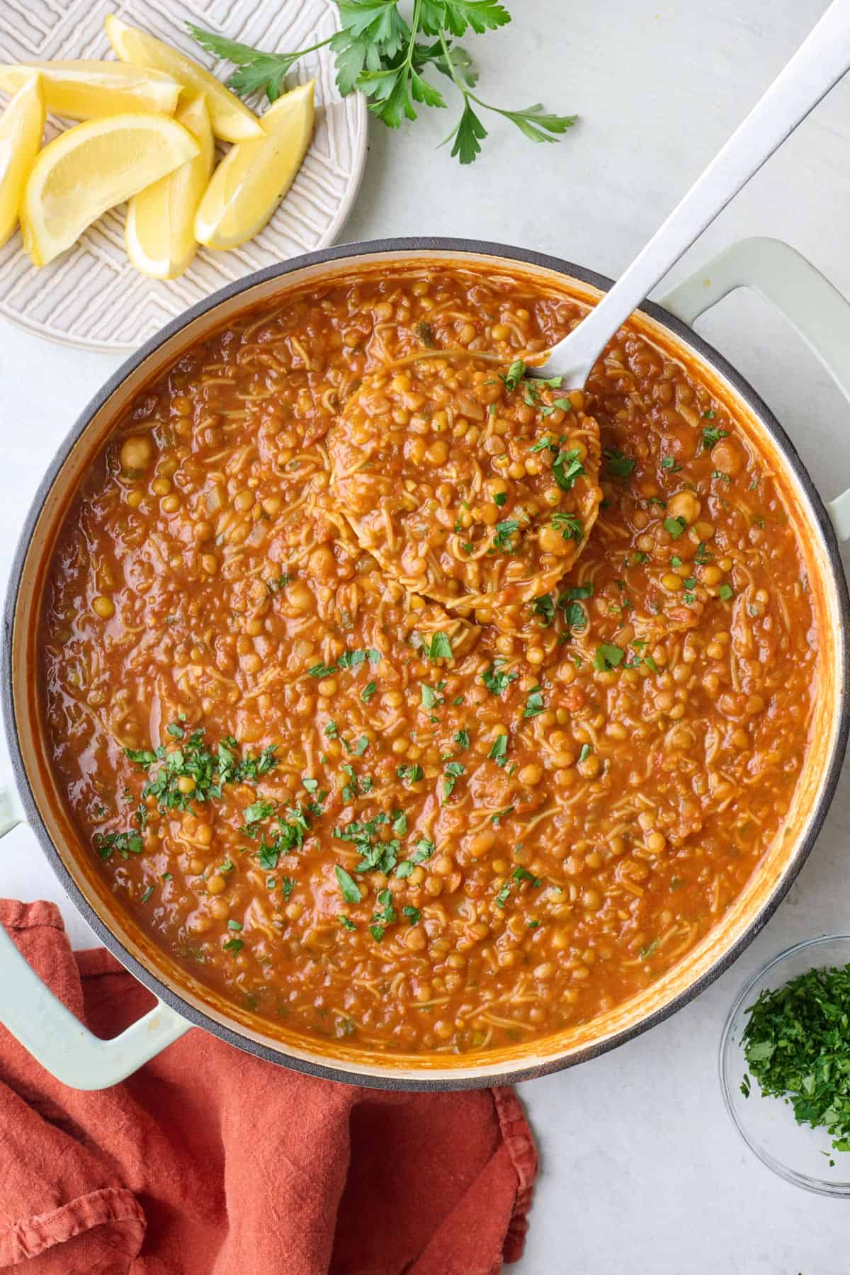 Harira lentil soup in pot with ladle dipped inside, fresh parsley and lemon nearby.