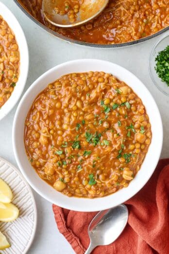 2 bowls of soup with spoon nearby, garnished with fresh parsley with pot in the corner.