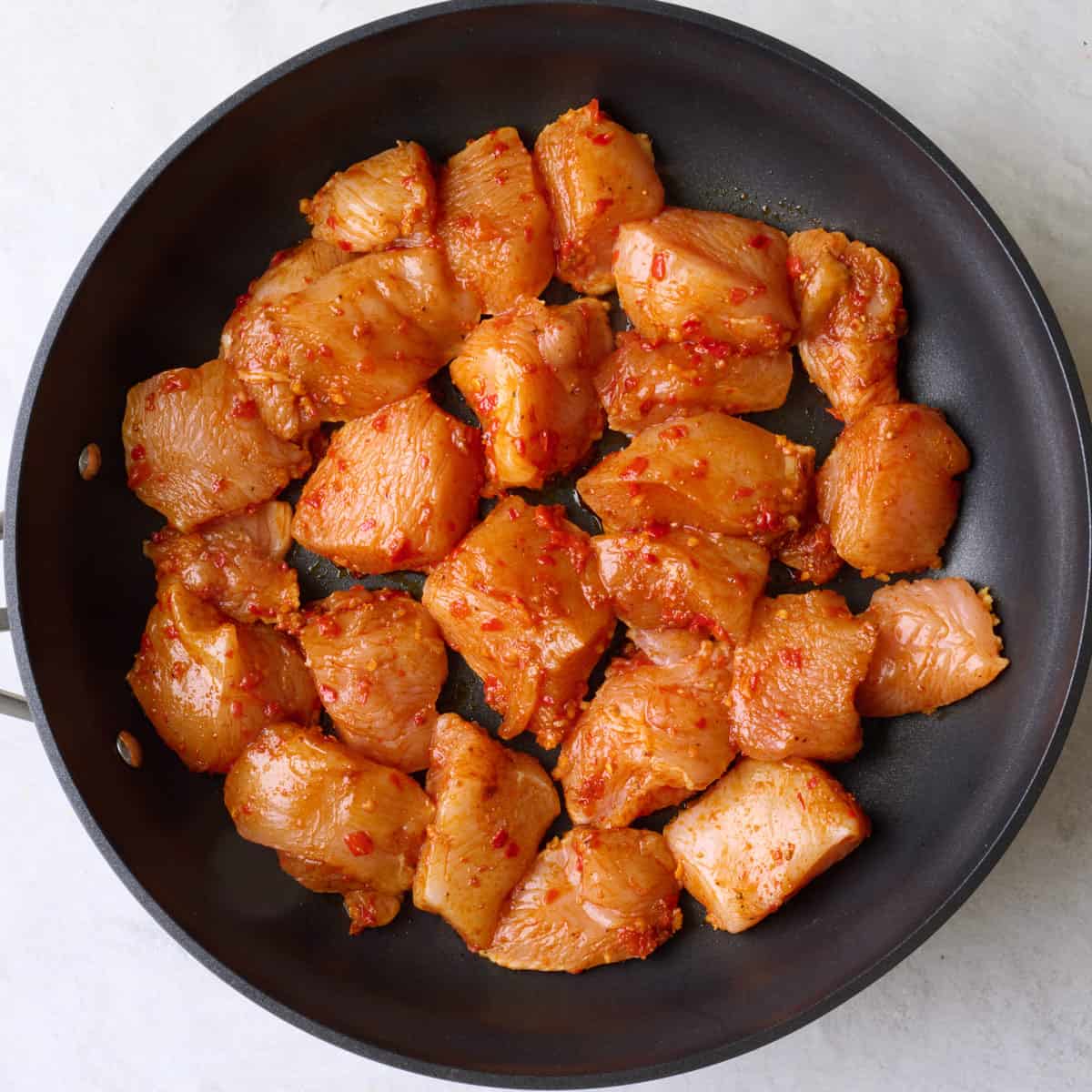 Marinated chicken pieces in a skillet.