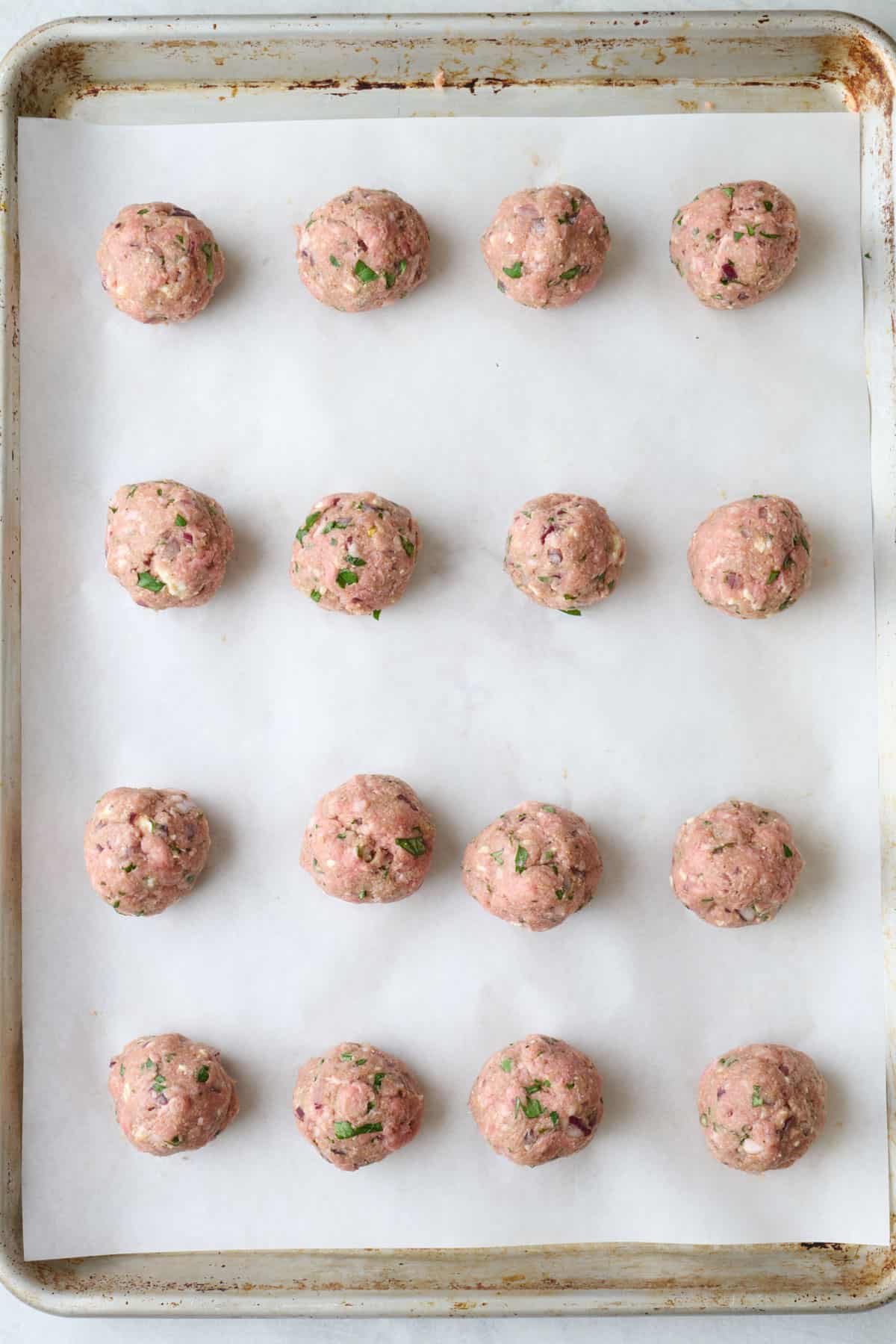 Meatballs scooped onto a parchment lined baking sheet before baking.