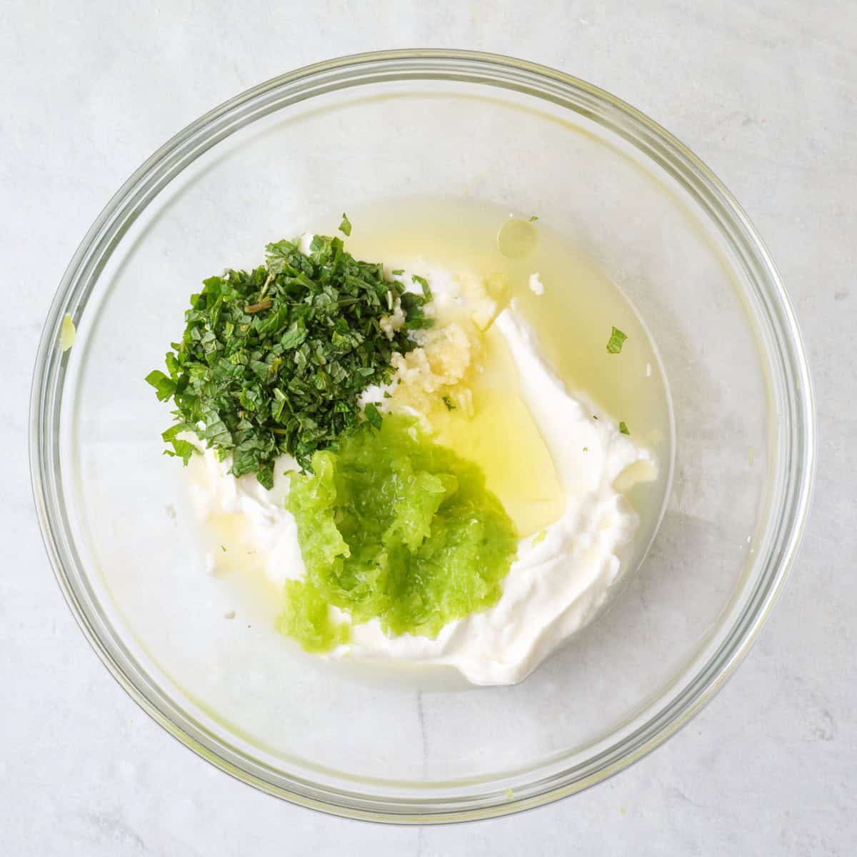 Strained grated cucumber, yogurt, garlic, juice, oil, mint and salt in a bowl.