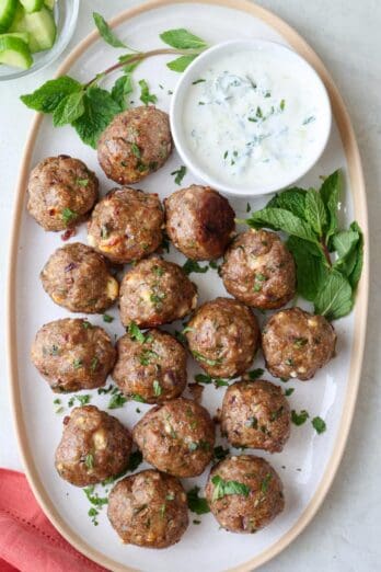 Lamb meatballs on a large plate with side of mint tzatziki sauce, garnished with extra fresh mint.