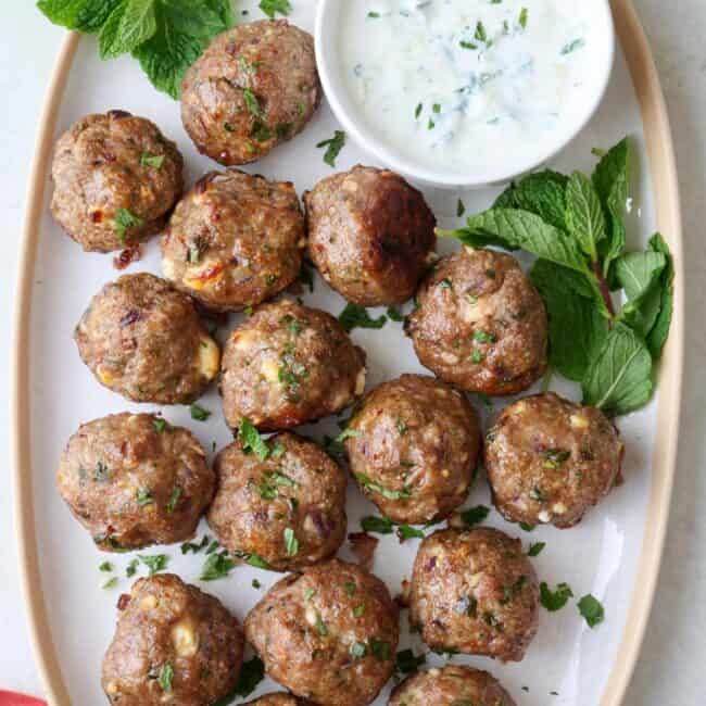 Lamb meatballs on a large plate with side of mint tzatziki sauce, garnished with extra fresh mint.