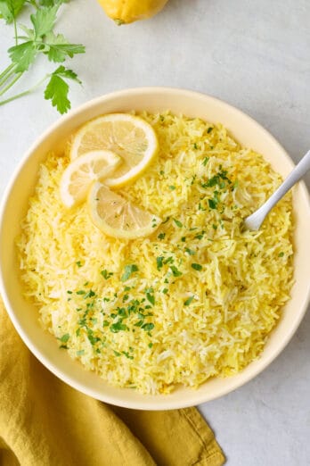 Lemon rice in a large serving bowl with serving spoon resting in bowl, garnished with fresh parsley and lemon slices.