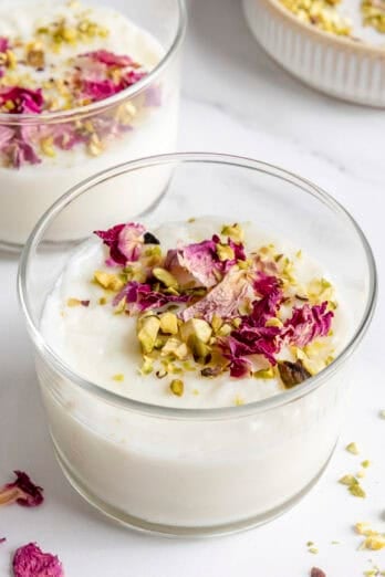 Serving of milk pudding, also called Muhallabia, in a small glass garnished with dried rose petals and chopped pistachios.