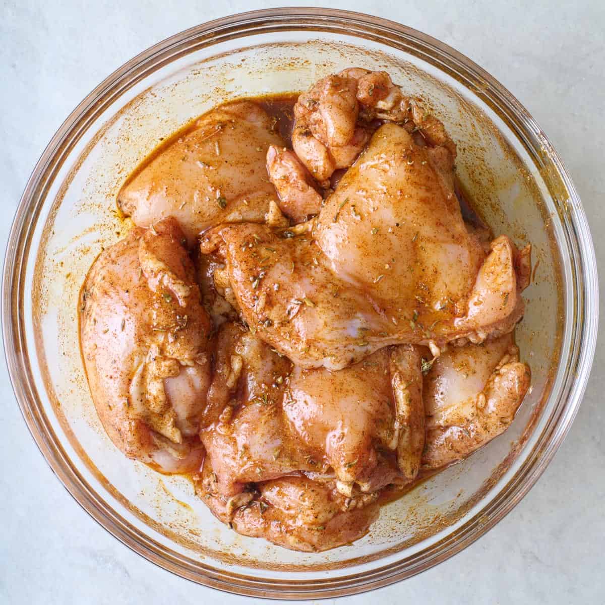 Boneless skinless chicken thighs tossed in marinade in a bowl.