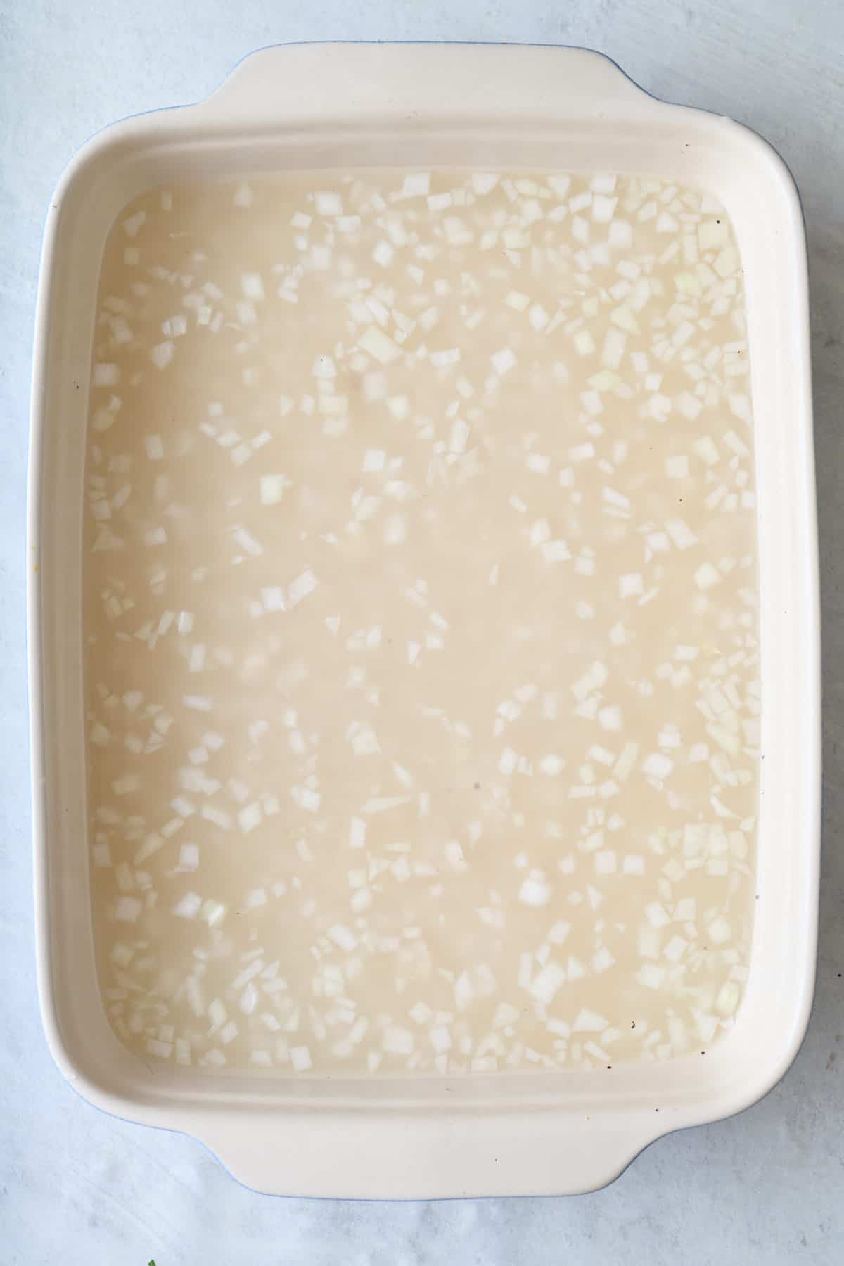 Rice, oil, onion in a baking dish with water.