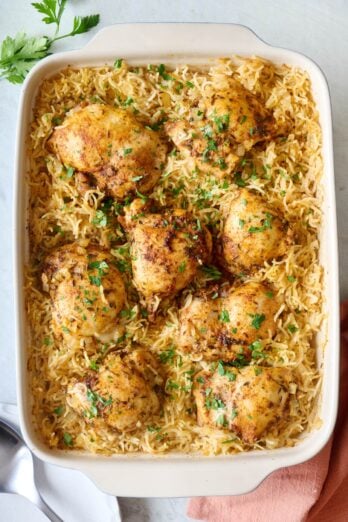 Oven baked chicken thighs and basmati rice in a baking dish garnished with fresh parsley.