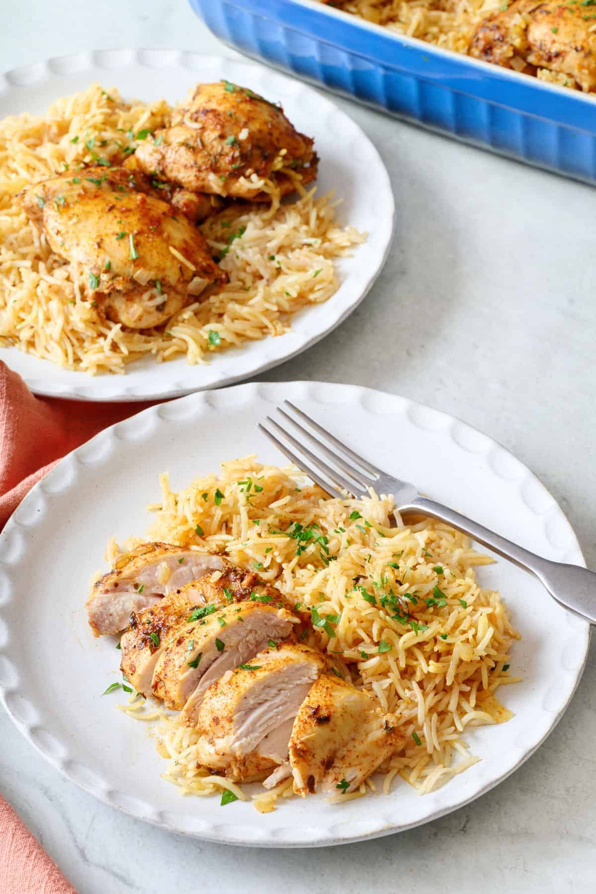 Two plates of chicken and rice with chicken sliced on one plate.