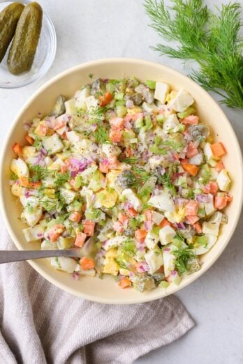 Crunch pickle salad in a serving bowl with fresh dill and dill pickles nearby.