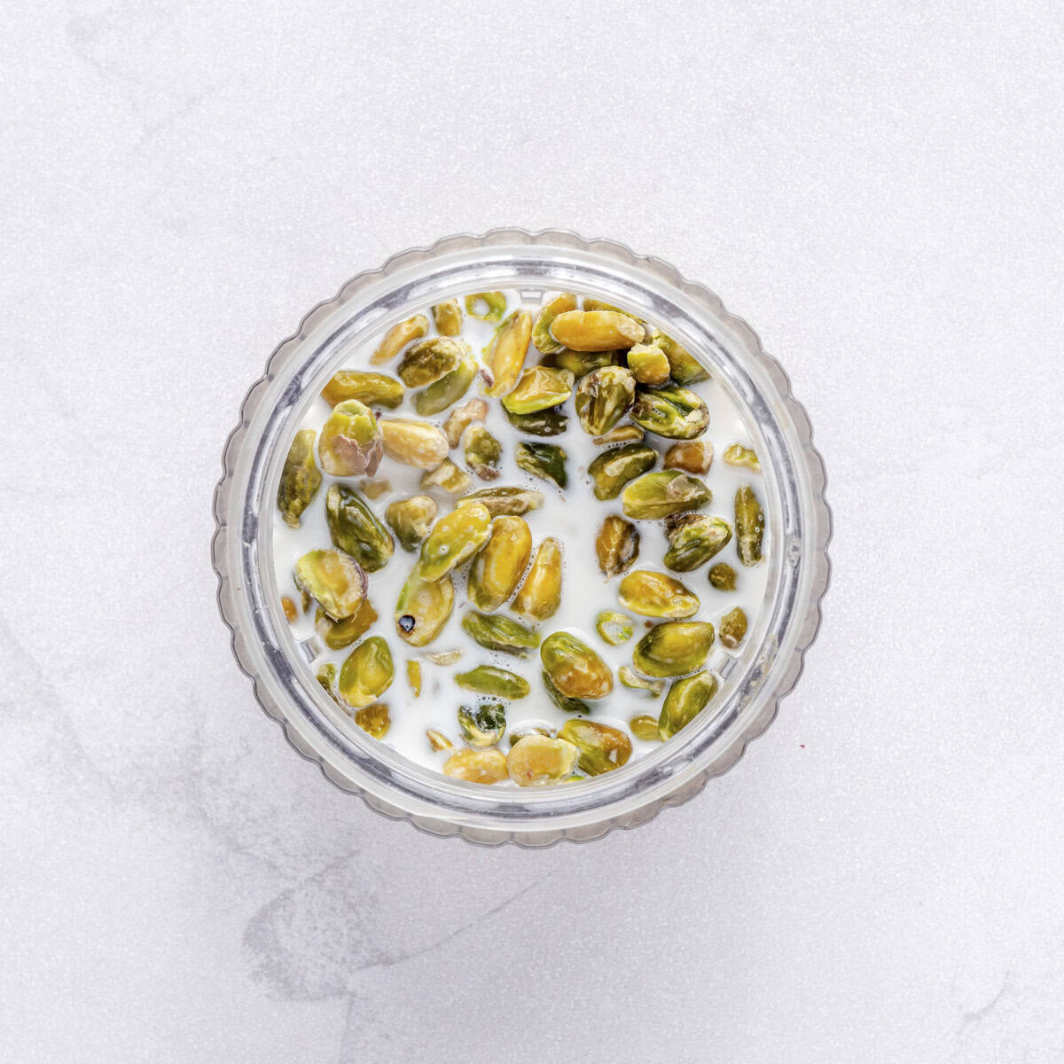 Skinned pistachios in the bowl of a food processor with warm milk.