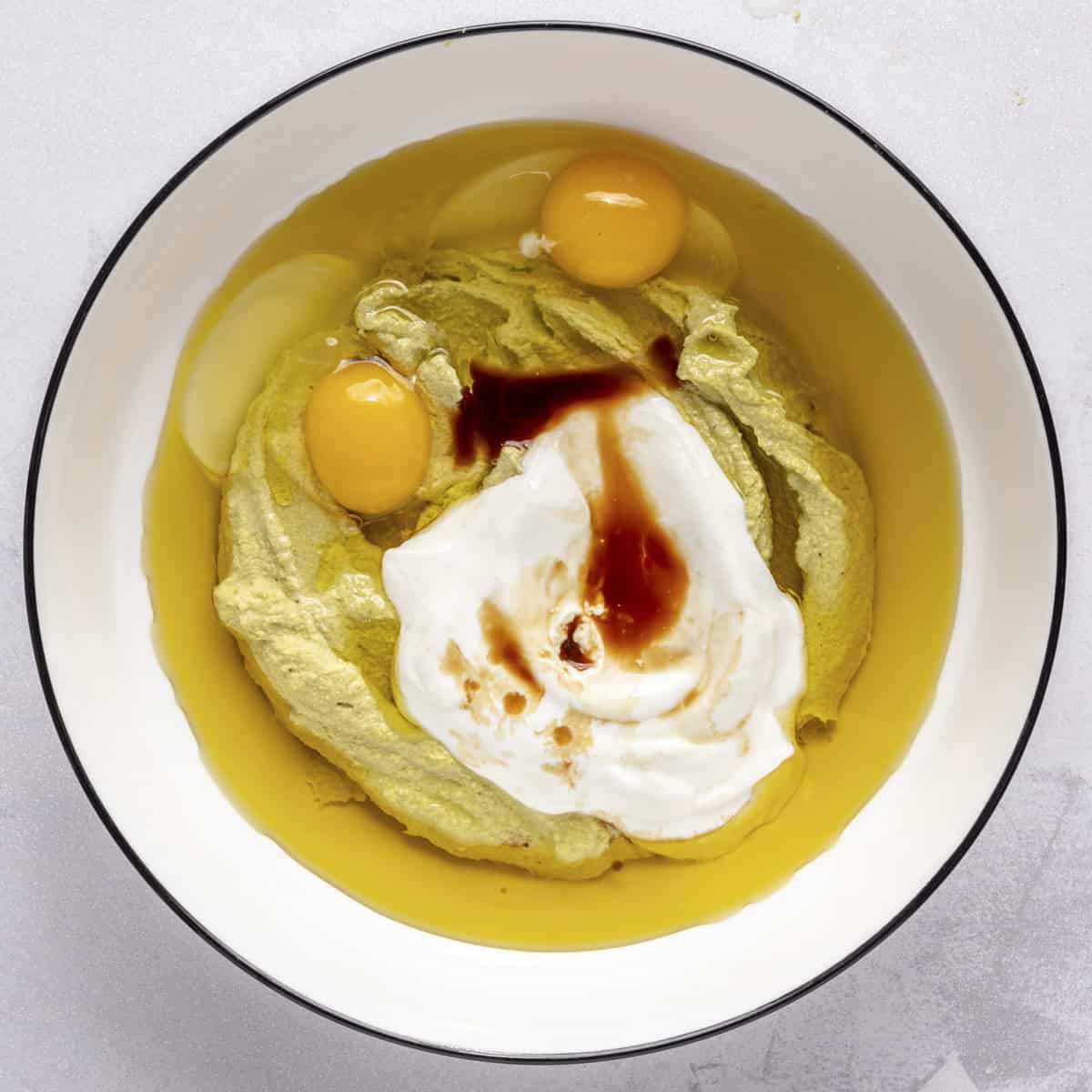 Pistachio butter, oil, eggs, yogurt and vanilla in a bowl.