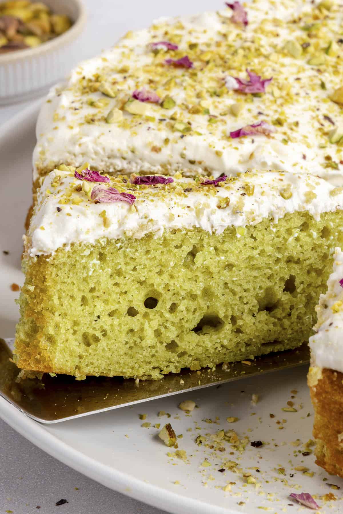 Slice of pistachio cake with cream cheese frosting being lifted away from cake.