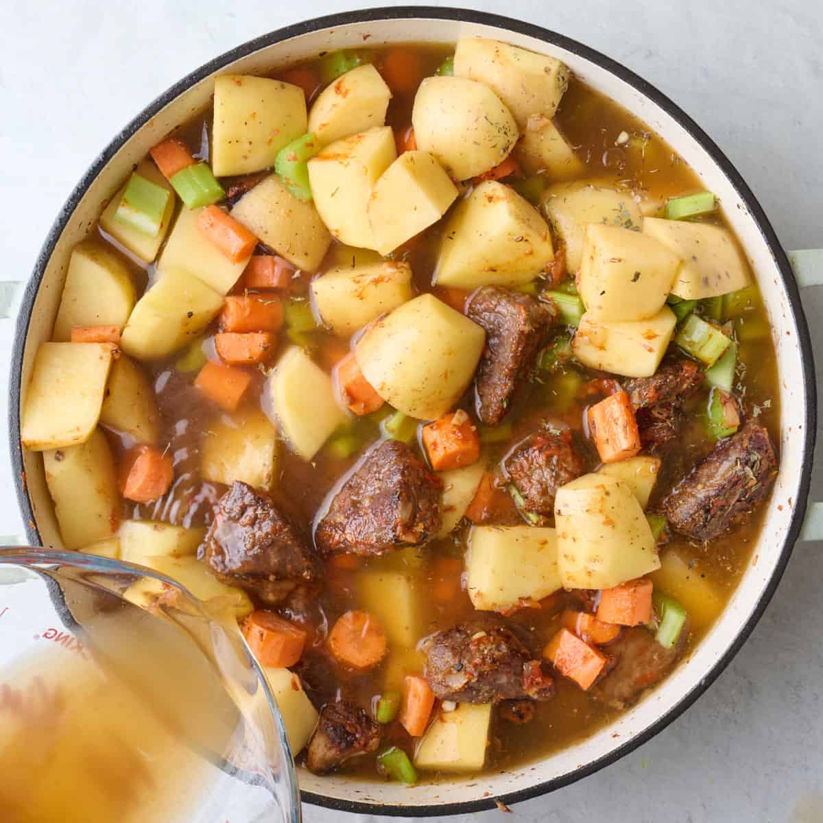 Adding broth to pot with beef and vegetables.