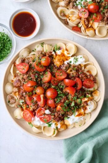 Two assembled bowls of turkish pasta with extra paprika butter sauce nearby.