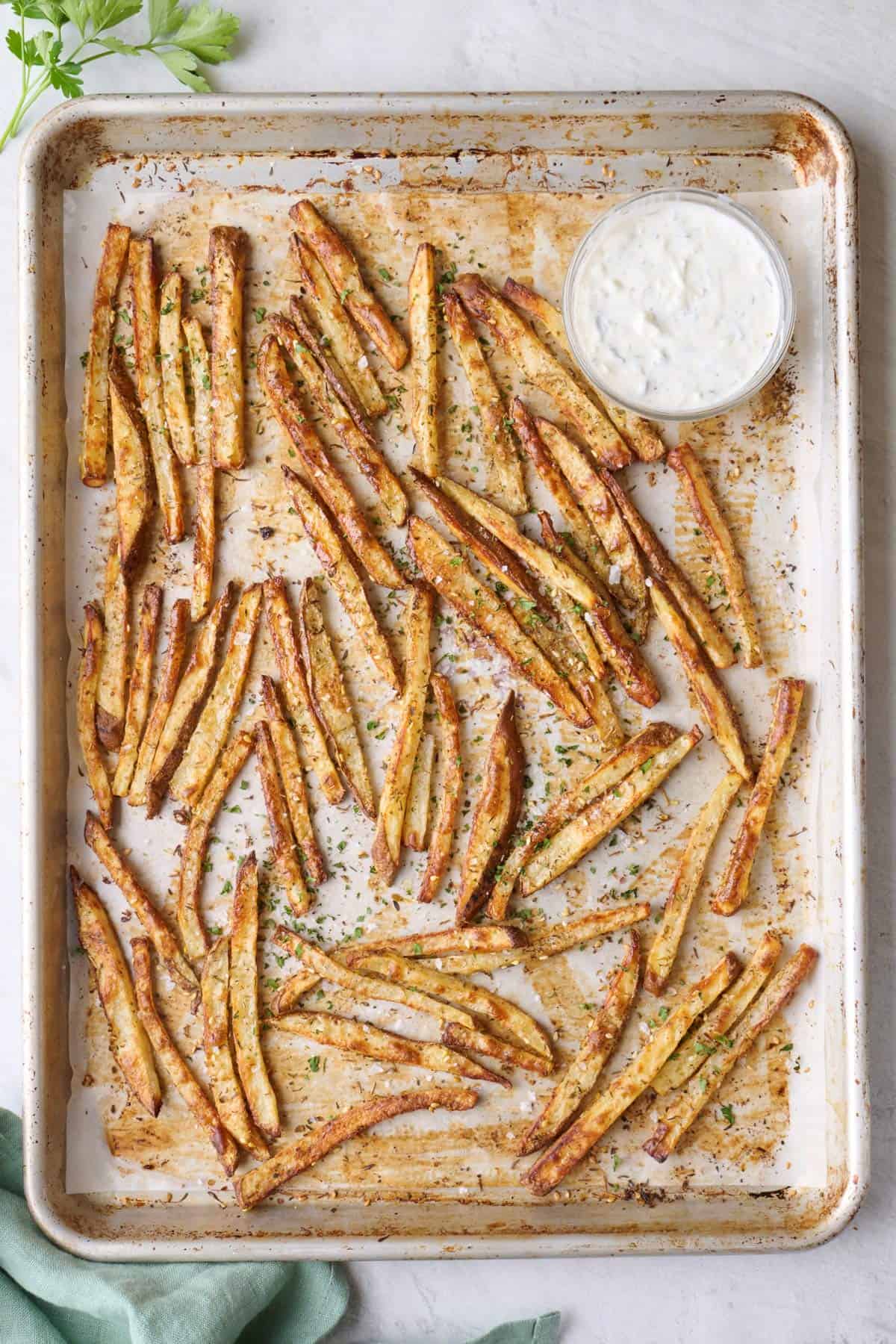 Zaatar fries on sheet pan garnished with flaky salt and fresh parsley, small dish of tahini yogurt sauce nearby.