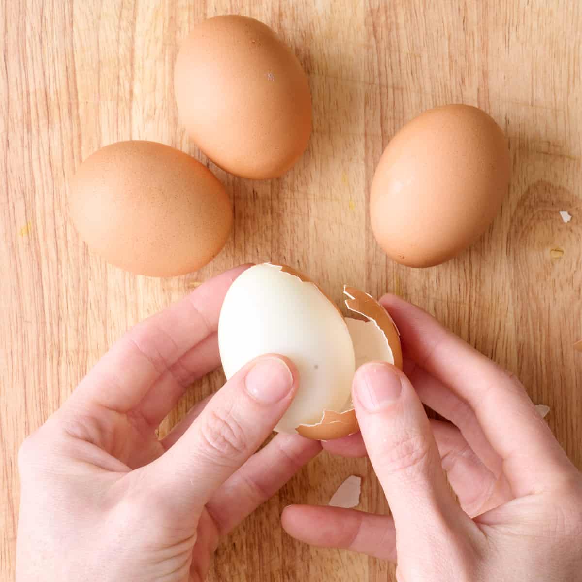 Hands peeling shell off a boiled egg.