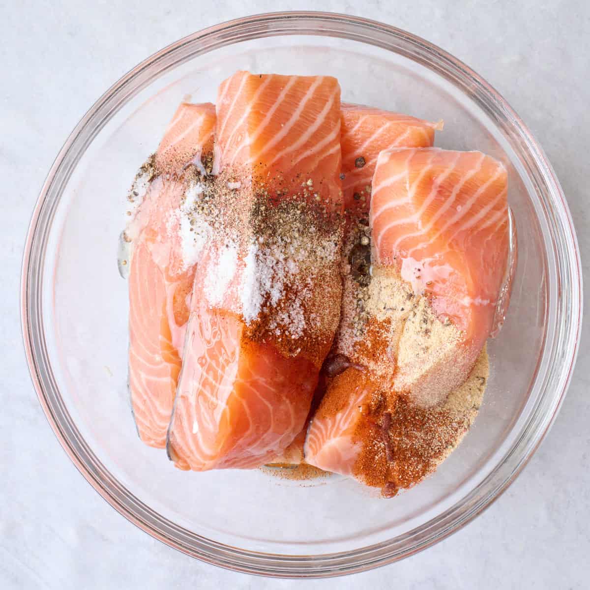 Salmon in a large bowl with oil, garlic powder, paprika, salt and pepper.