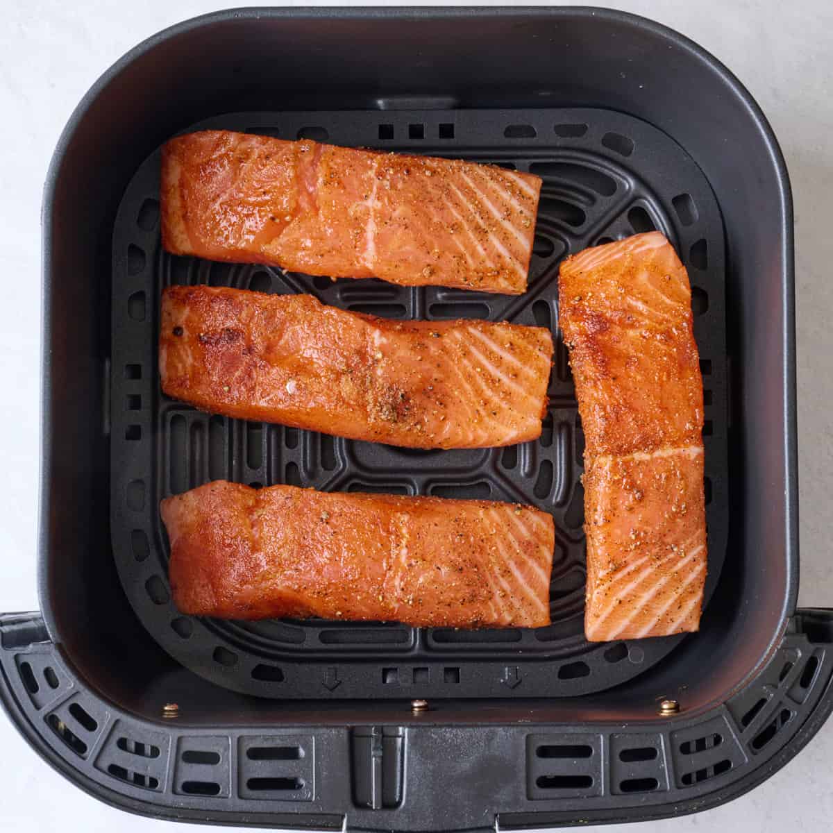 Seasoned salmon in an air fryer basket before cooking.