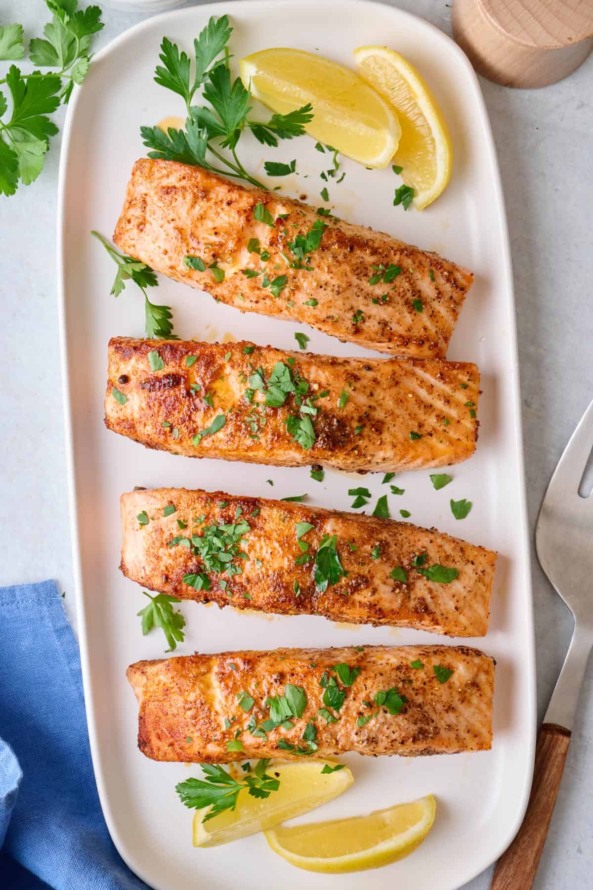 Salmon fillets on a platter with garnish, and serving fork resting nearby.