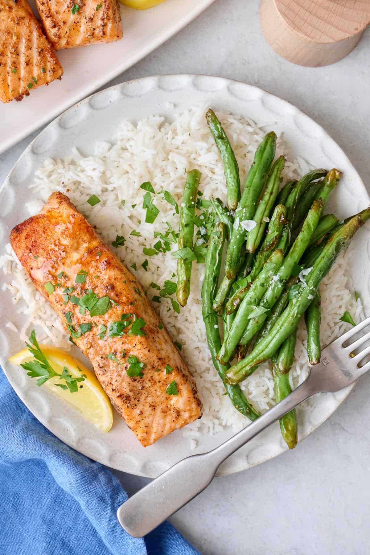 Seasoned salmon fillet on a plate served over rice with green beans.