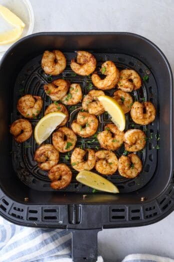 Air fryer shrimp in basket garnished with fresh parsley and lemon wedges.
