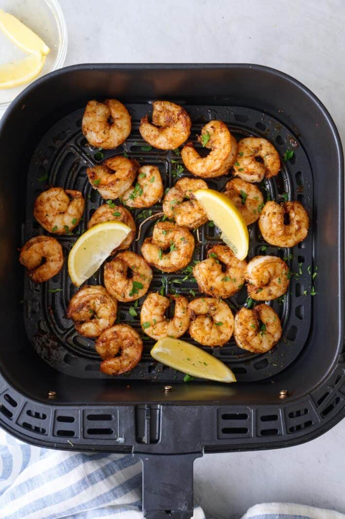 Air fryer shrimp in basket garnished with fresh parsley and lemon wedges.