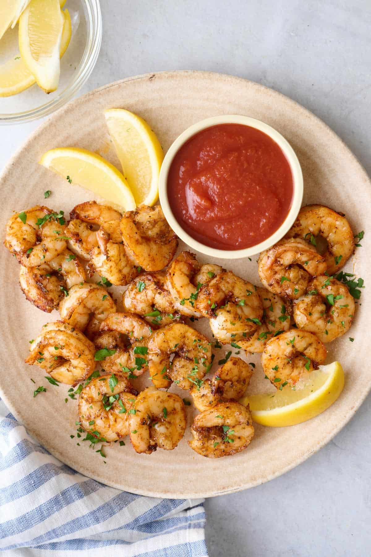 A plate of air fryer shrimp with cocktail sauce and lemon wedges.