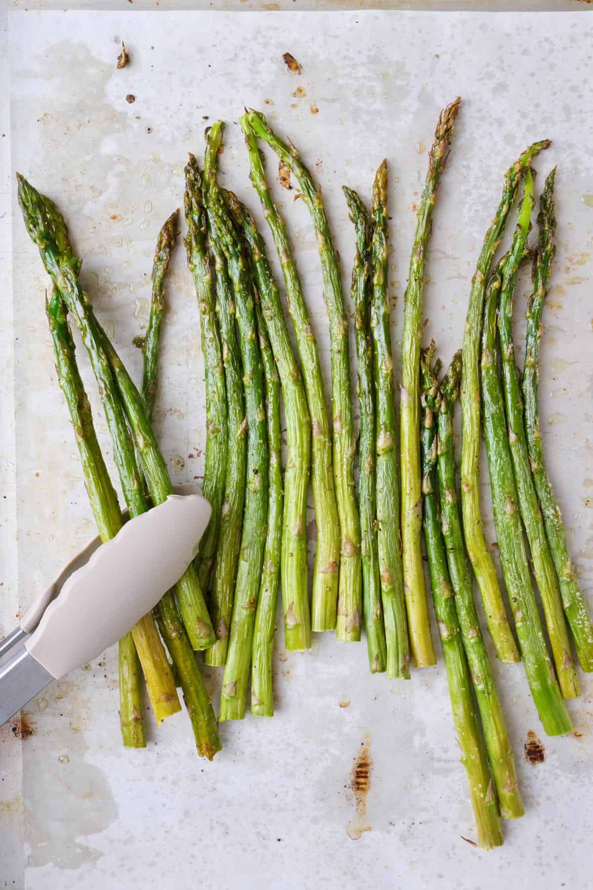 Tongs lifting up asparagus form sheet pan.
