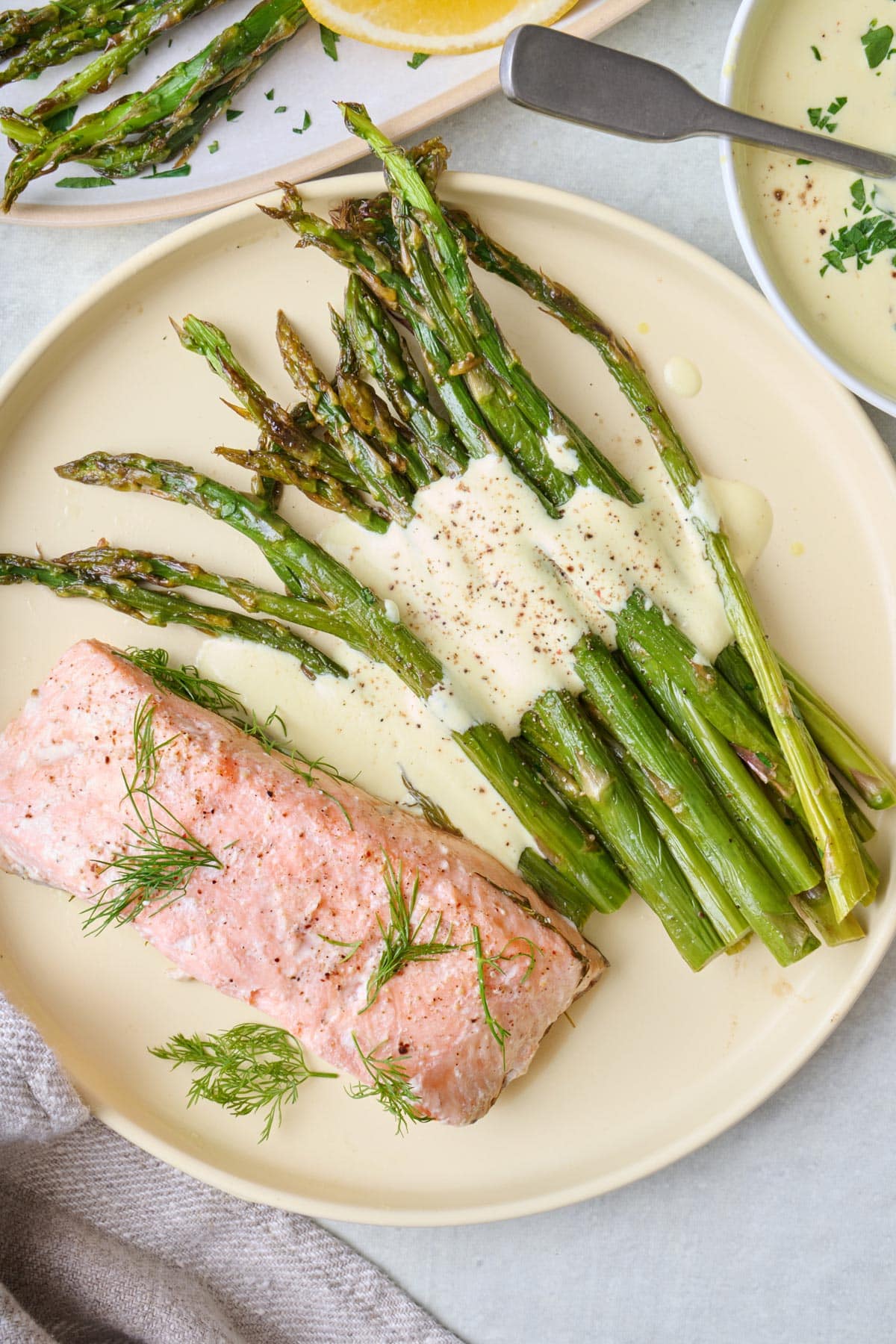 Baked asparagus on a plate with hollandaise sauce on top and served with poached salmon.