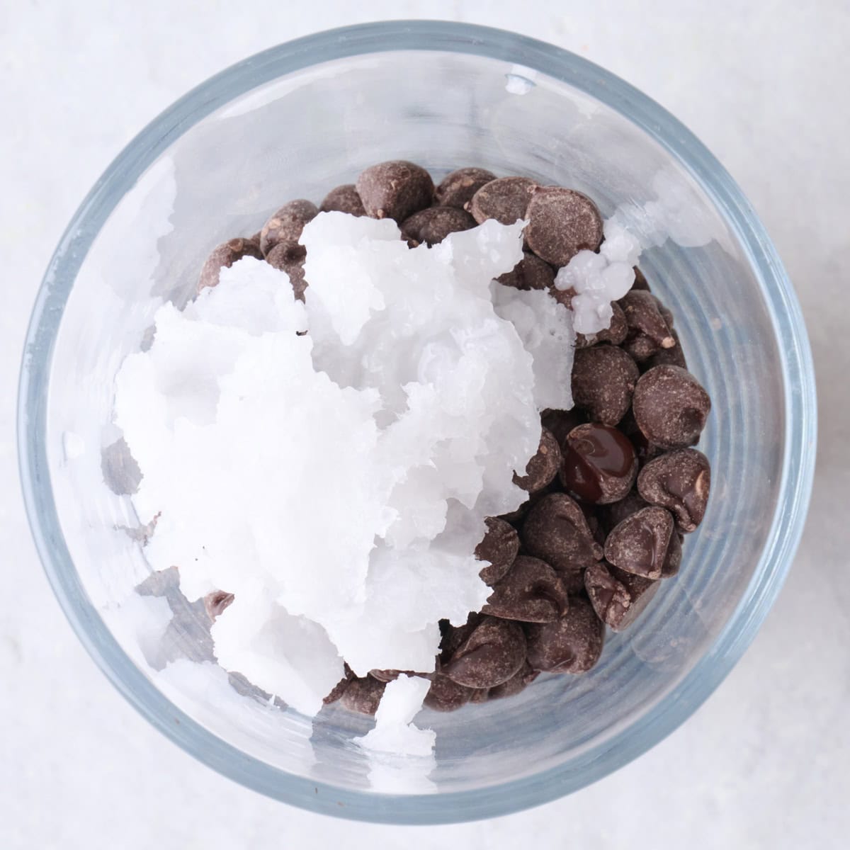 Chocolate chips and coconut oil in a tall glass.