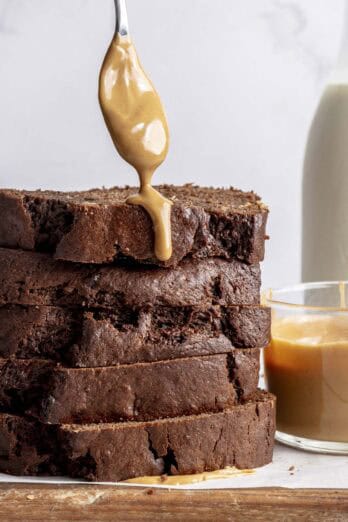 Stack of sliced chocolate peanut butter banana bread with a spoon drizzling it with peanut butter.