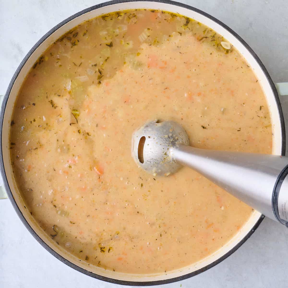 Immersion blender dipped inside soup, slightly blended.