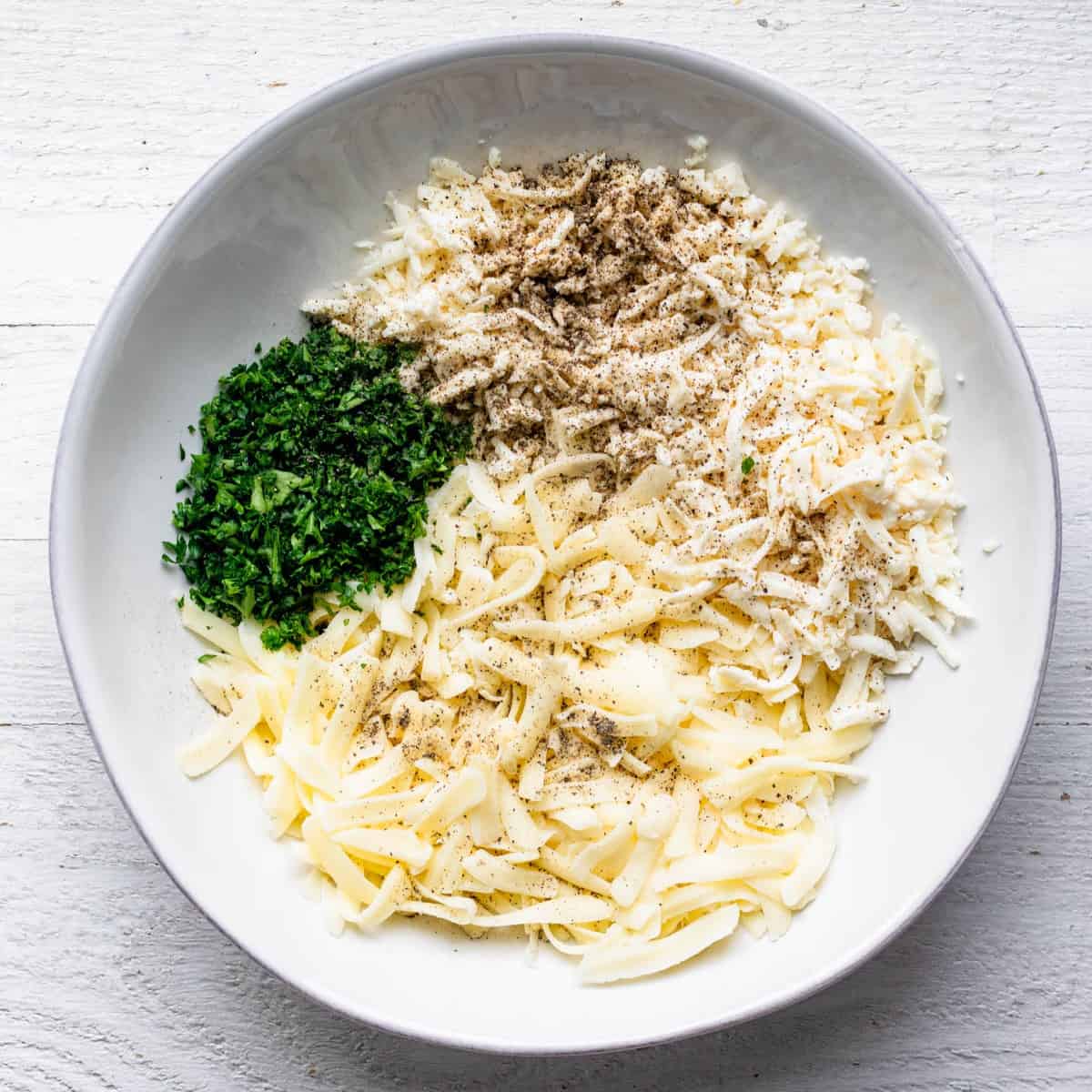 Cheeses, herbs, and spices in a bowl before mixing.