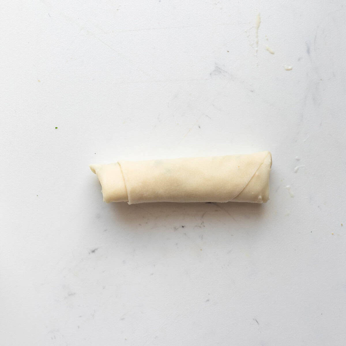Spring roll wrapper filled with cheese after rolling.
