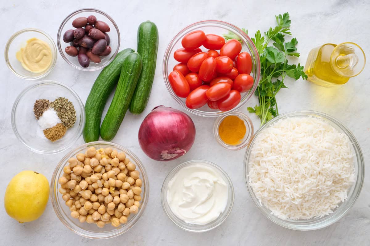 Ingredients for recipe before prepping: kalamata olives, persian cucumbers, red onion, grape tomatoes, chickpeas, rice, Dijon mustard, lemon, spices, yogurt, parsley and yogurt.