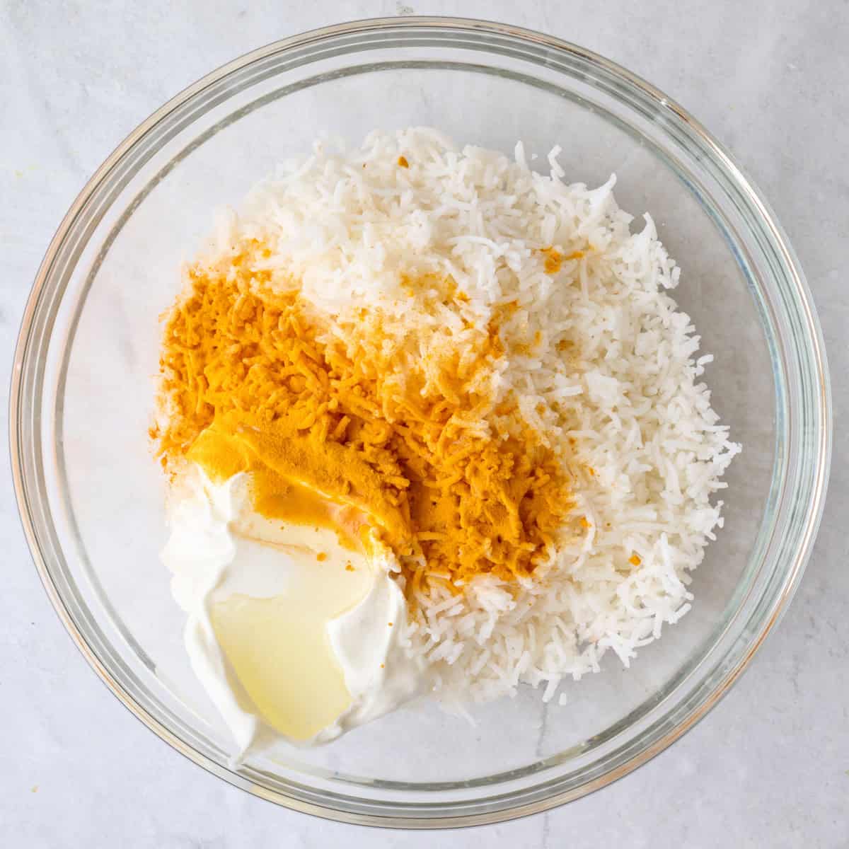 Cooked rice in a bowl with greek yogurt, olive oil, and turmeric.