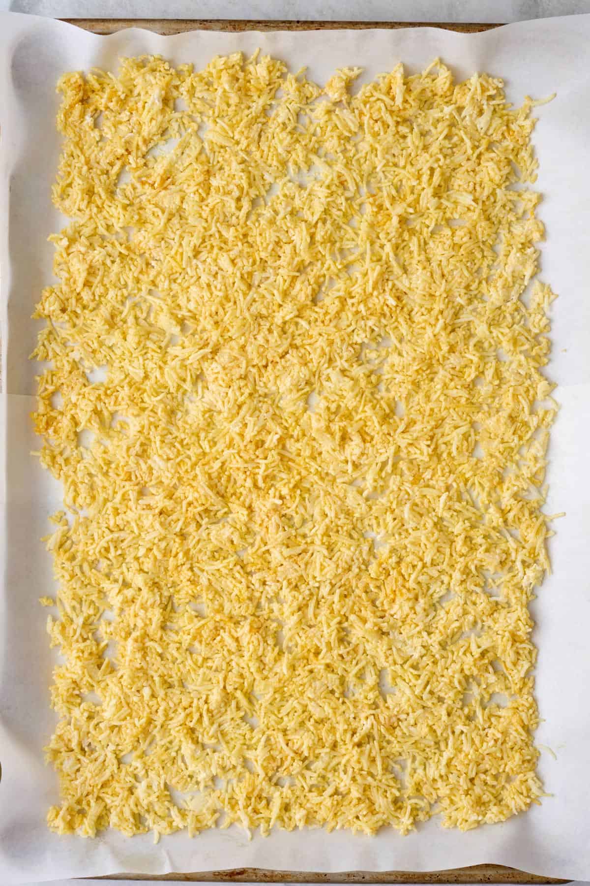 Seasoned rice spread out on a parchment line baking sheet.