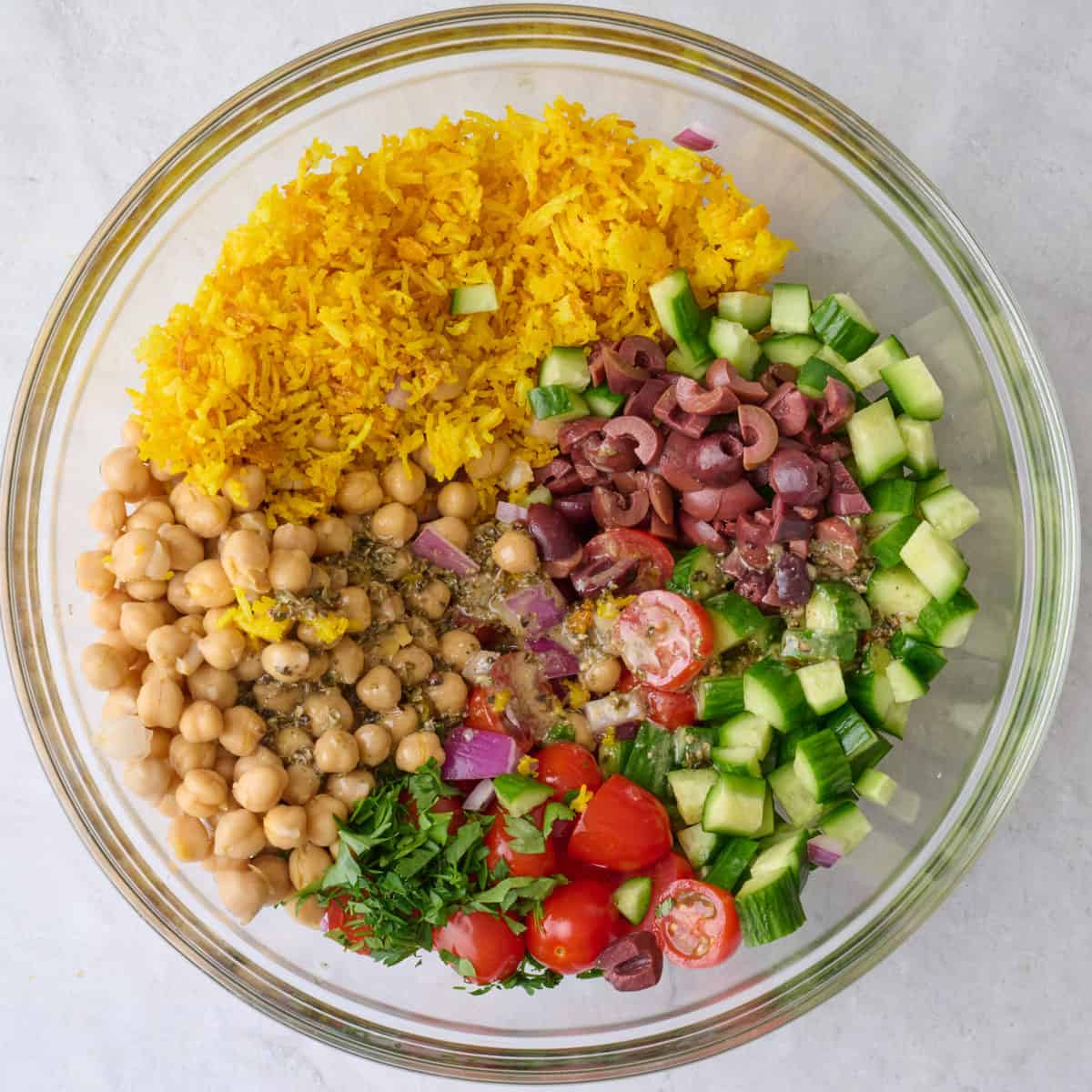 Large bowl with chickpeas, cucumbers, tomatoes, red onion, olives, parsley, rice and dressing before mixing.