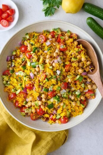 Crispy rice salad recipe in a shallow serving bowl with a wooden spoon dipped inside and extra fresh veggies around.