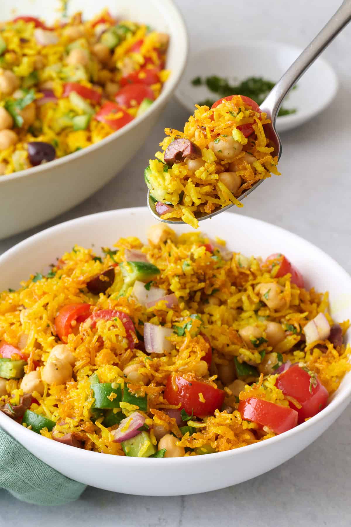 Spoon lifting up a bite of crispy yellow rice salad with chickpeas and fresh vegetables.