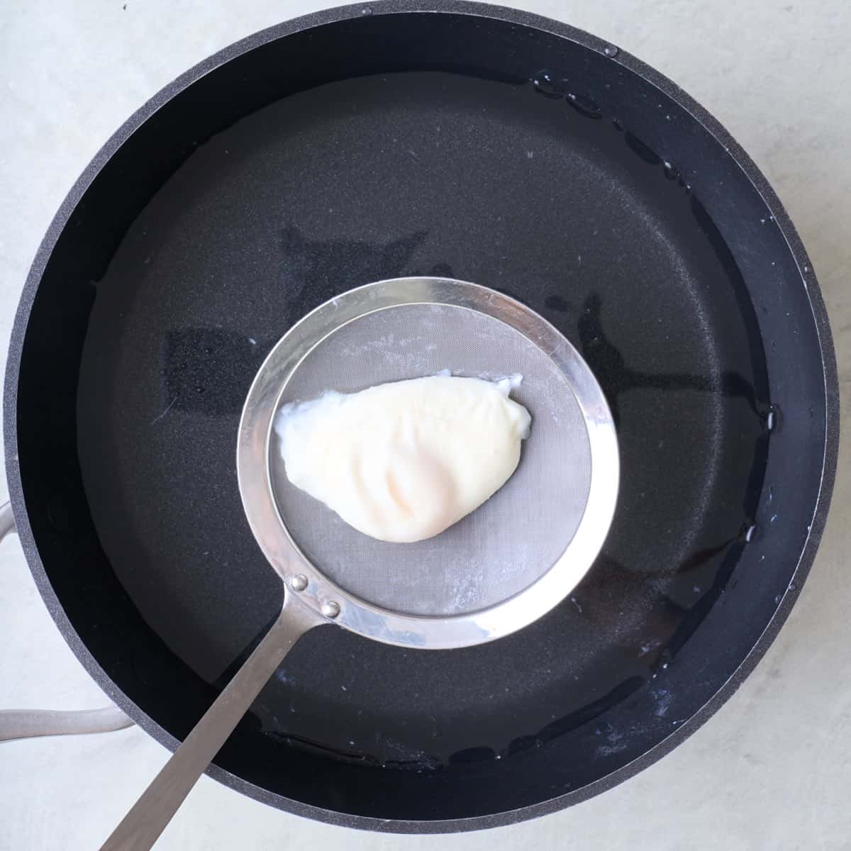 Mesh spoon lifting up poached egg.