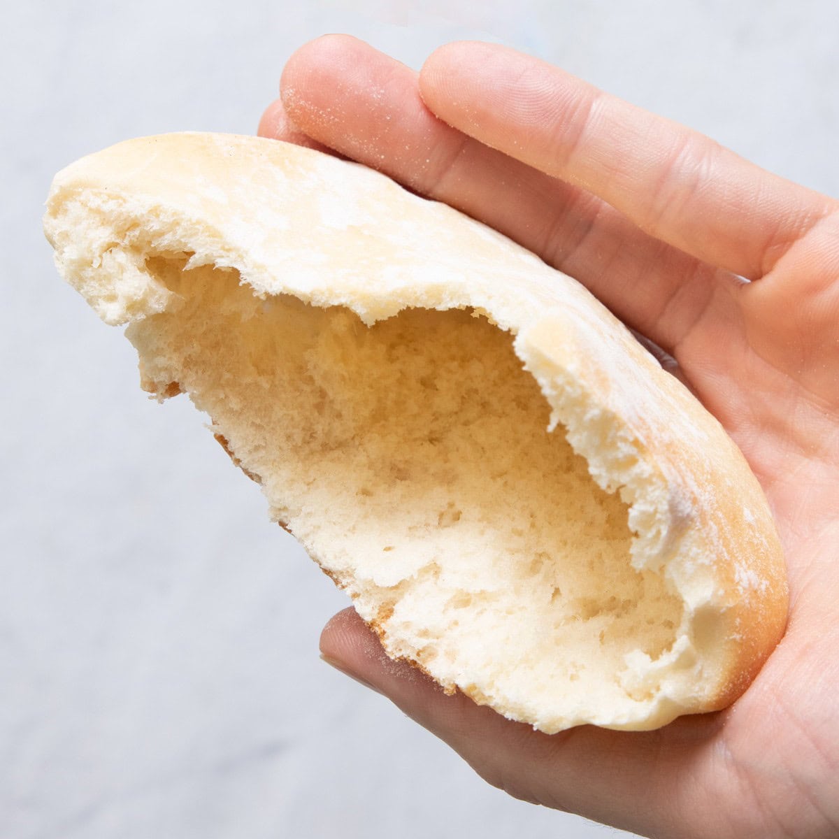 Hand holding a freshly baked pita bread, half torn away to show inside puffy texture.