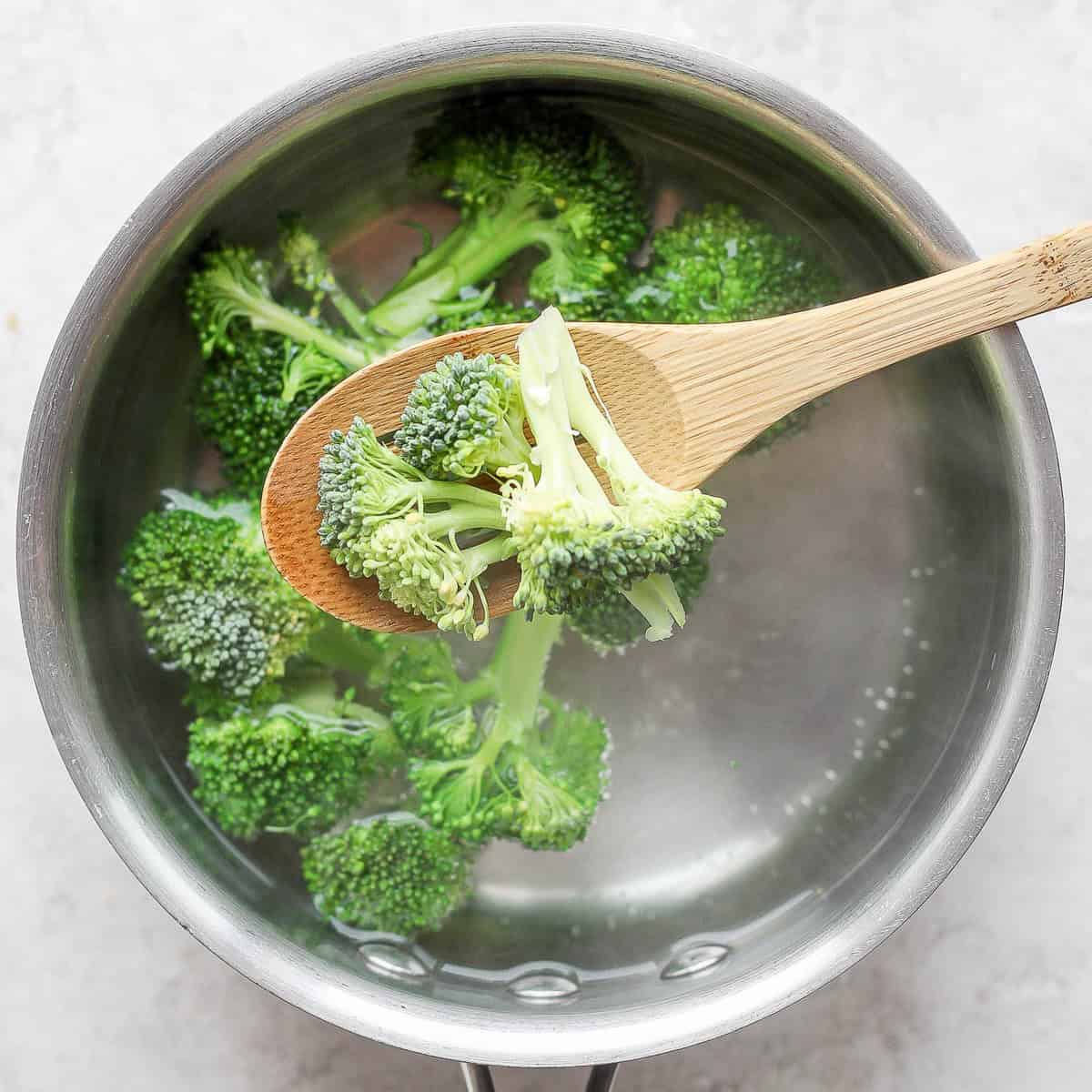 Spoon adding raw broccoli florets to a pot of water.