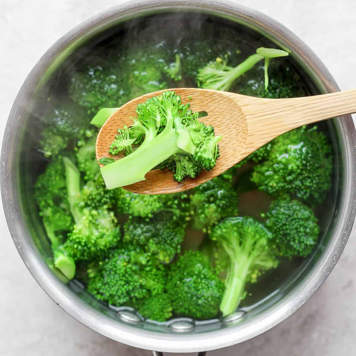 Spoon lifting up a cooked broccoli floret from a pot of hot water.
