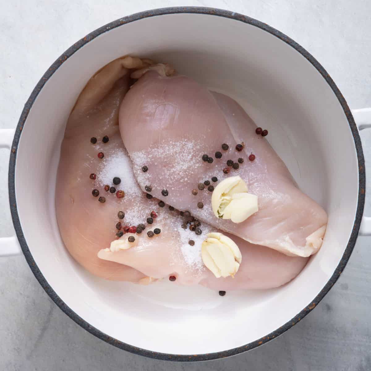 Chicken breasts in a pot with spices and crushed garlic.