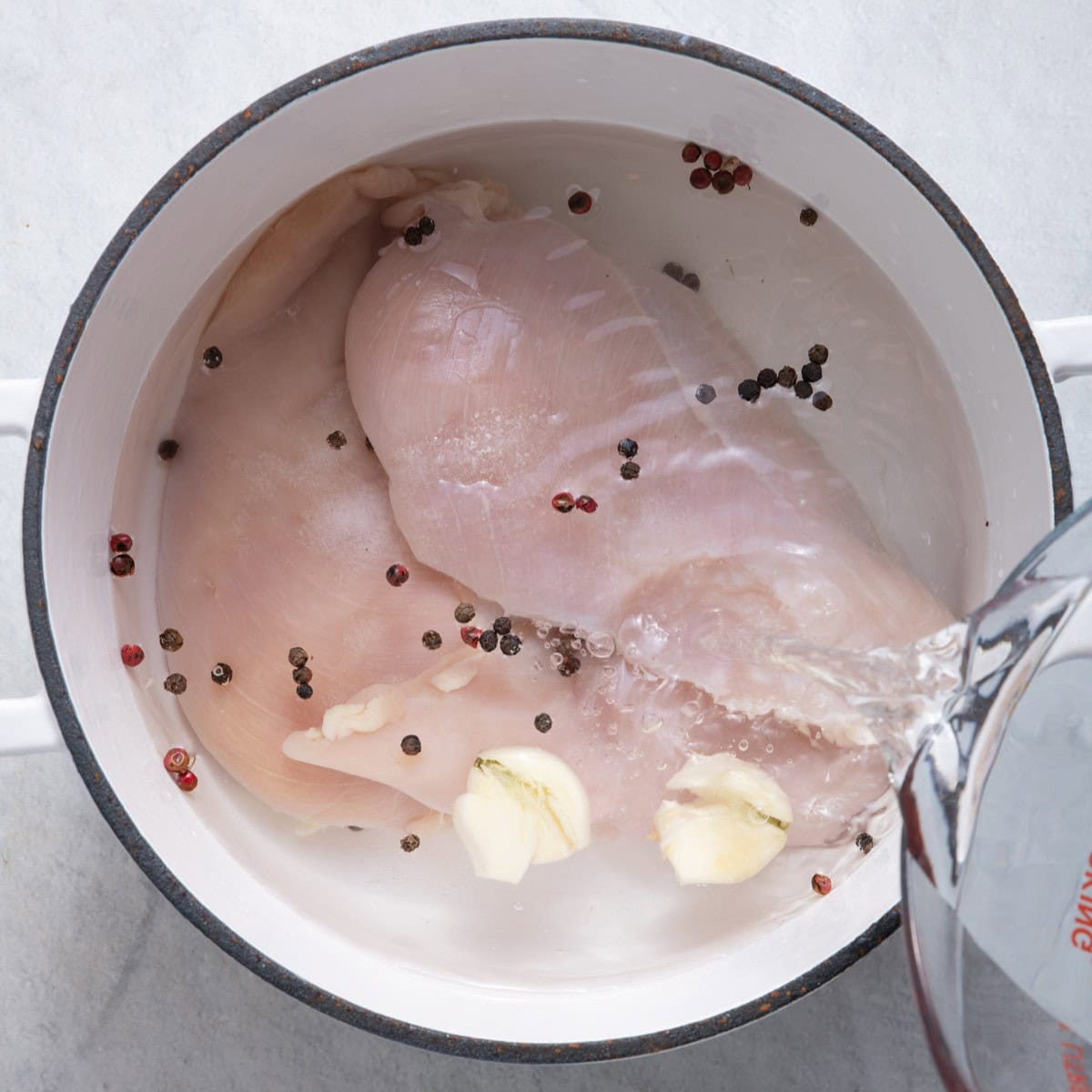 Water being added to pot of chicken breasts and seasonings.