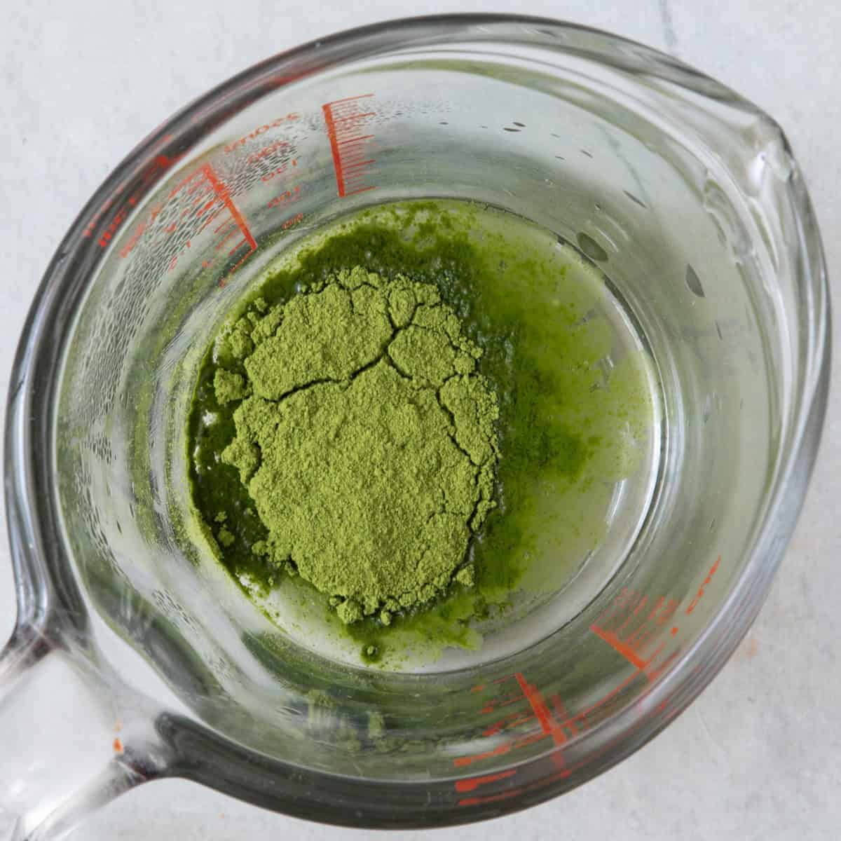 Measuring cup with matcha and hot water before whisking.