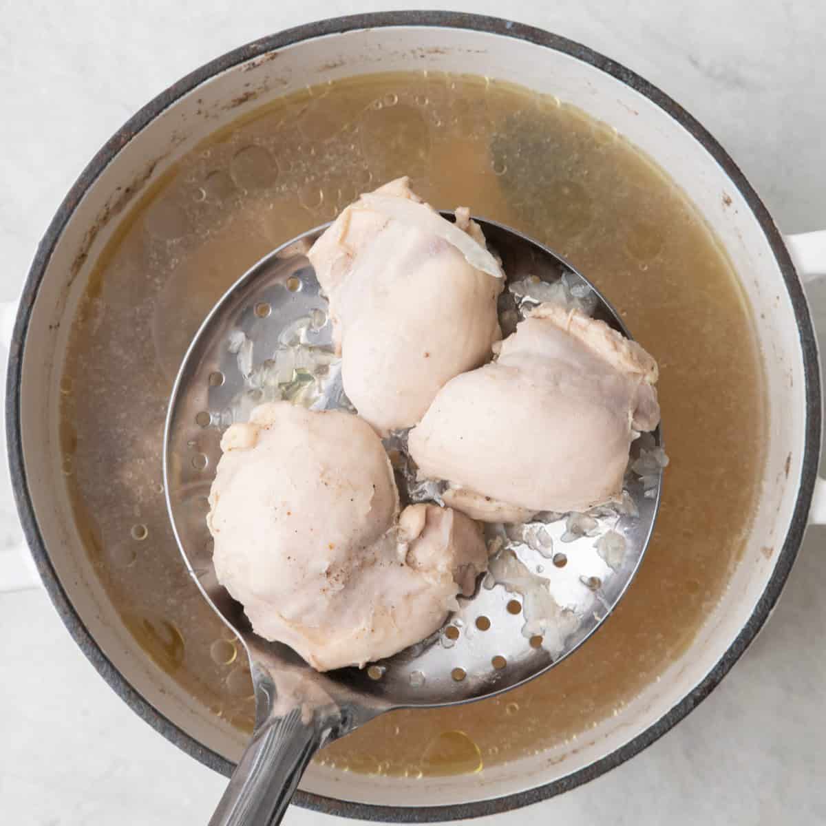Slotted spoon with chicken thigh coming out of pot.