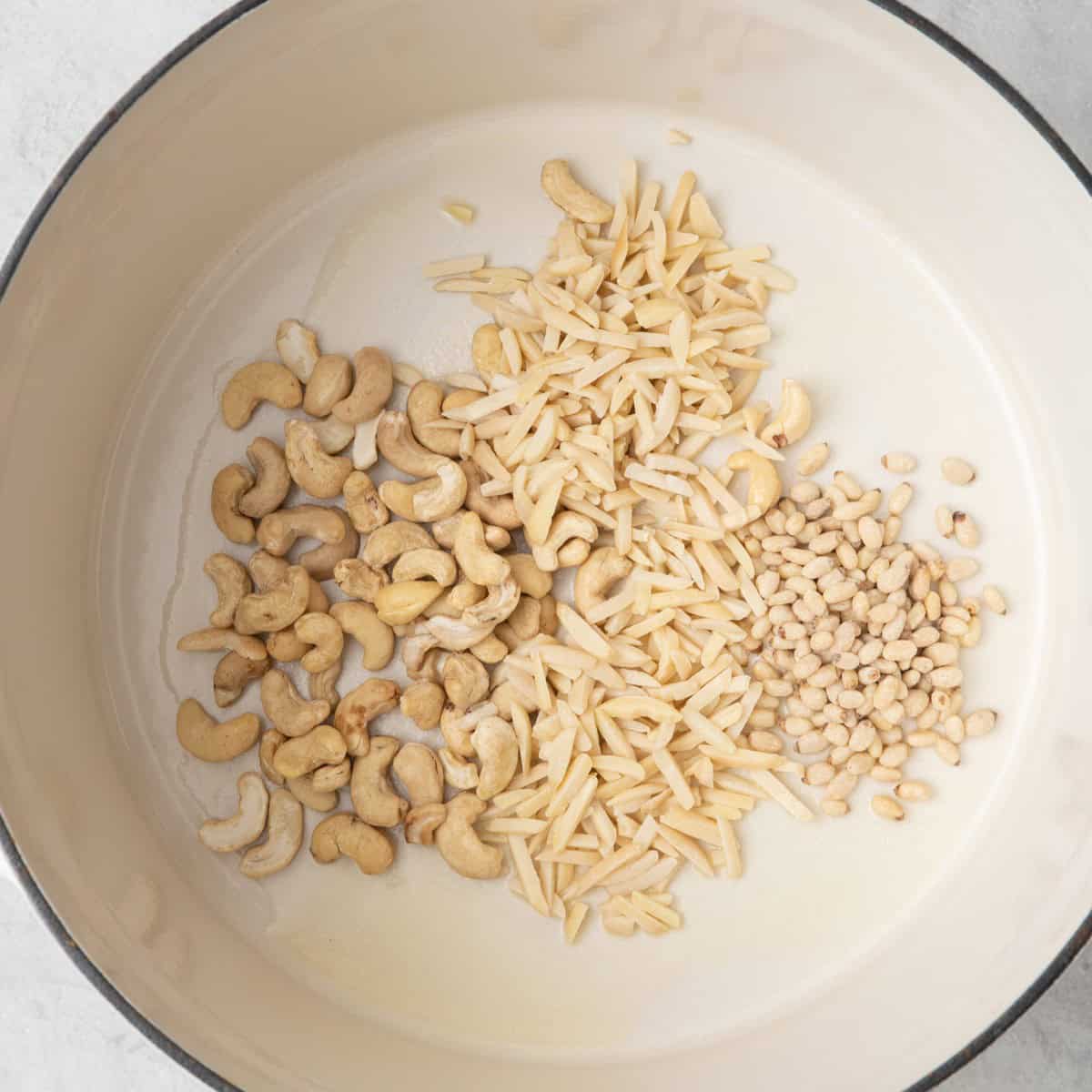 Cashews, almonds and pine nuts with melted butter in a large pot before toasting.